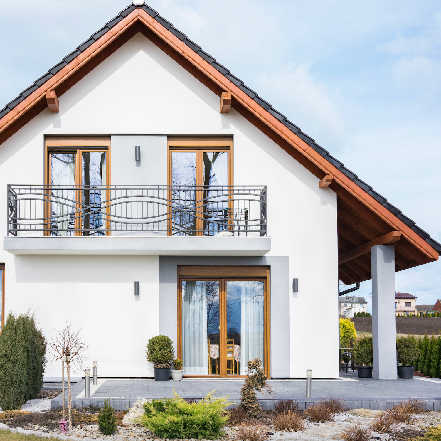 Modern house with white exterior, wooden French doors, and brown roof against a blue sky.