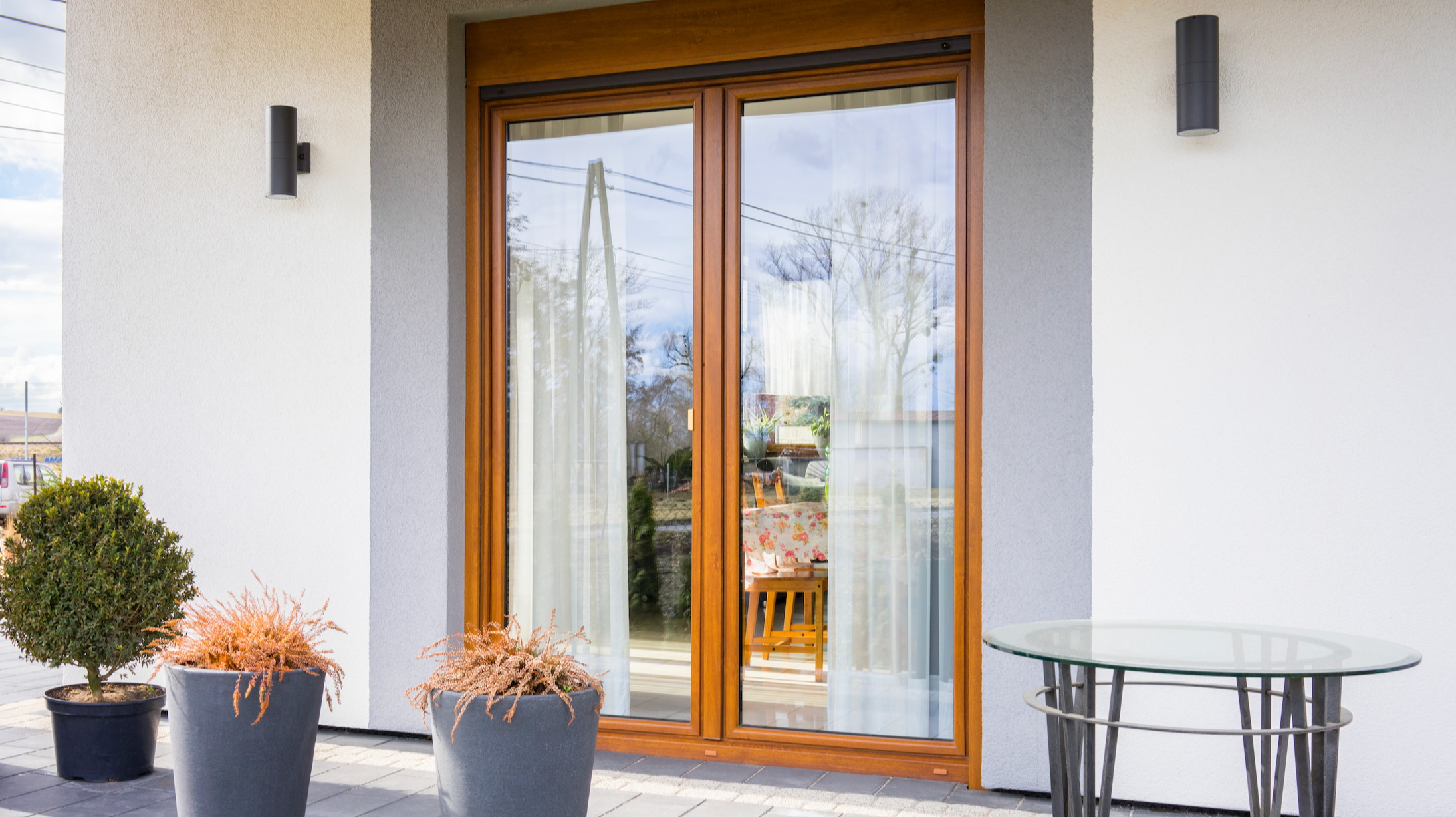 Modern patio with wooden French doors, outdoor furniture, and potted plants.