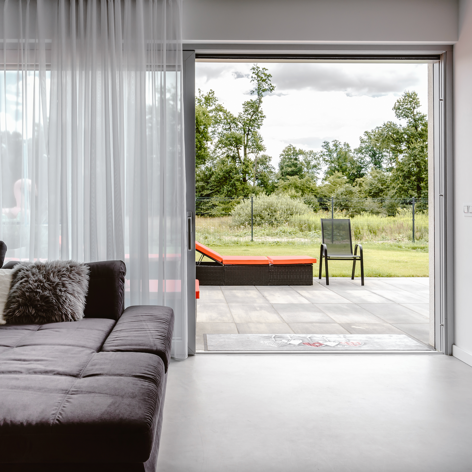 Modern living room with a large sectional sofa and a view of a garden through a glass patio door.