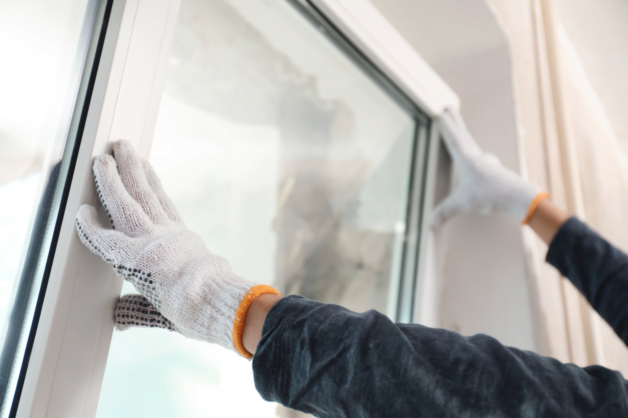 A worker fits a white tilt and turn window into a frame from the interior of a house.