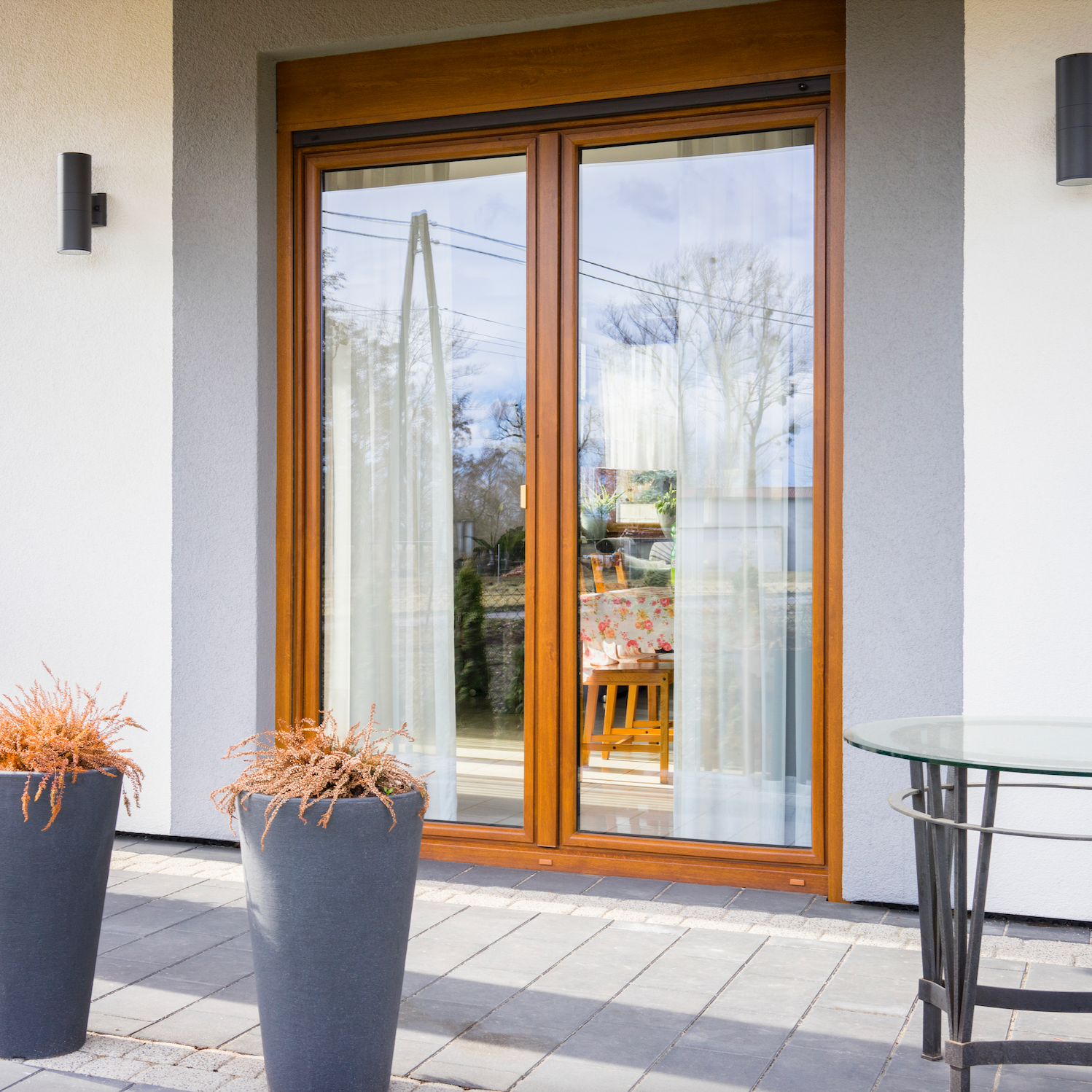 Modern patio with wooden French doors, outdoor furniture, and potted plants.
