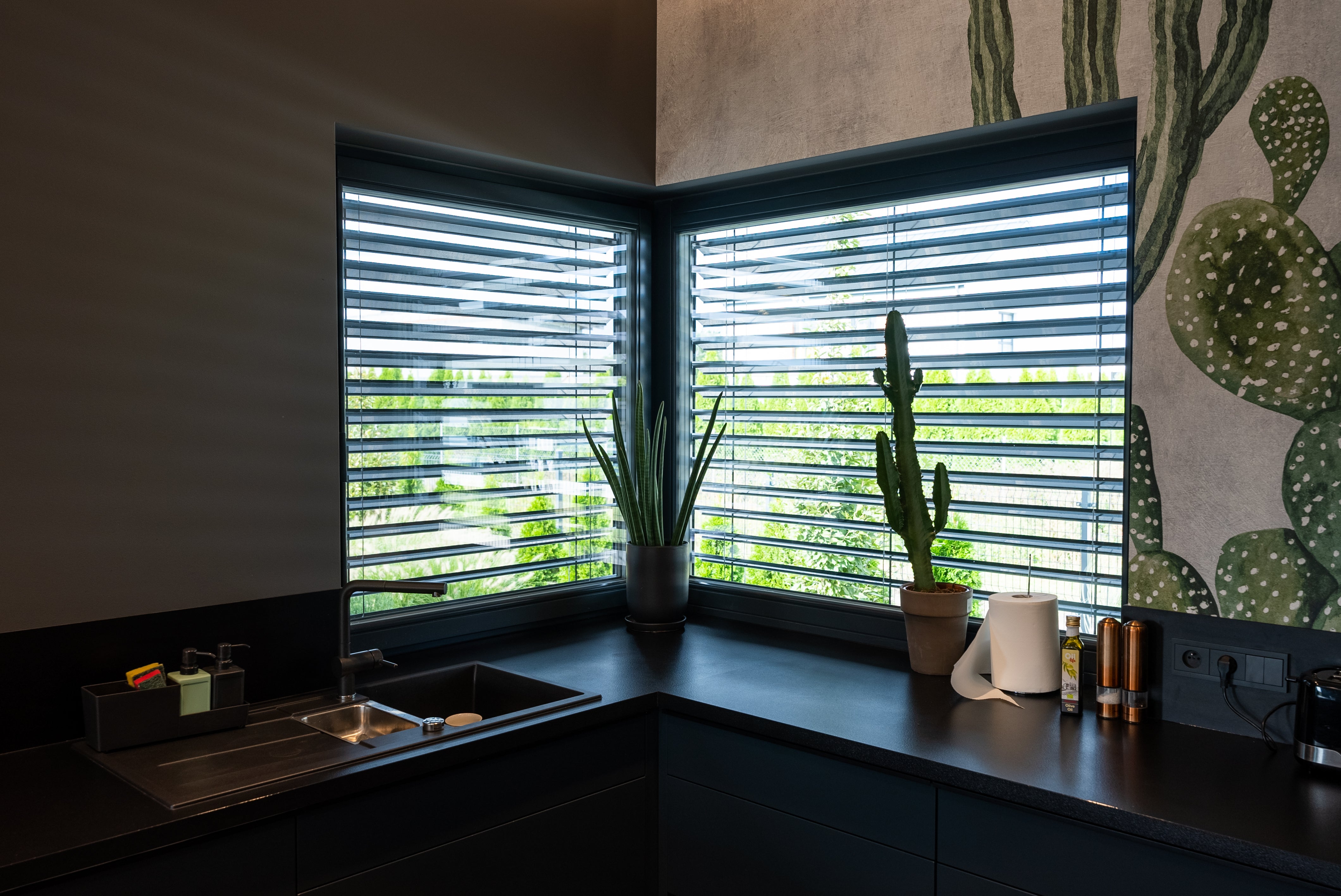 Modern kitchen with dark cabinets, a sink, and large windows with exterior venetian blinds.